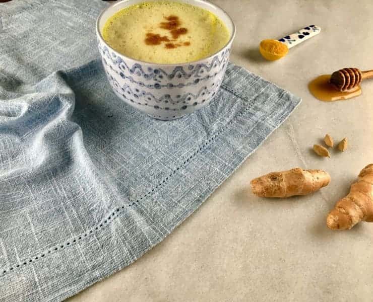A cup of ginger tea on a table next to a spoon.