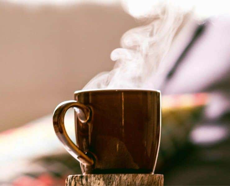 A steaming brown mug filled with a hot beverage is placed on a wooden surface, with a blurred background.