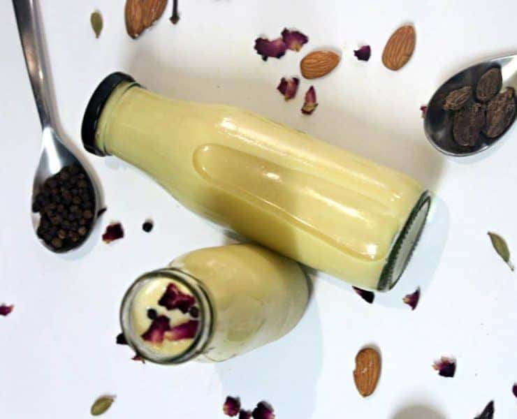 A jar of almond milk with a spoon and almonds.