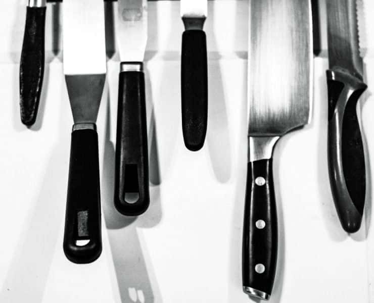 A row of black-handled kitchen knives hanging on a wall-mounted magnetic strip.