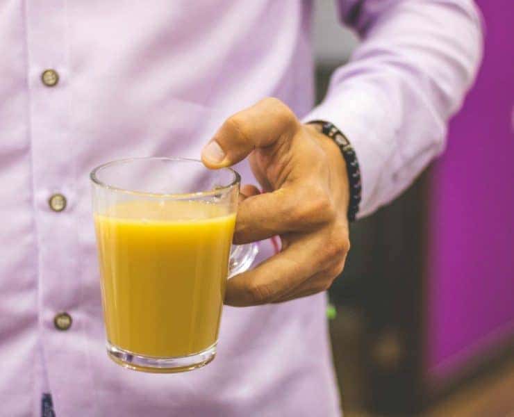A person in a light purple shirt holds a clear mug filled with orange juice.