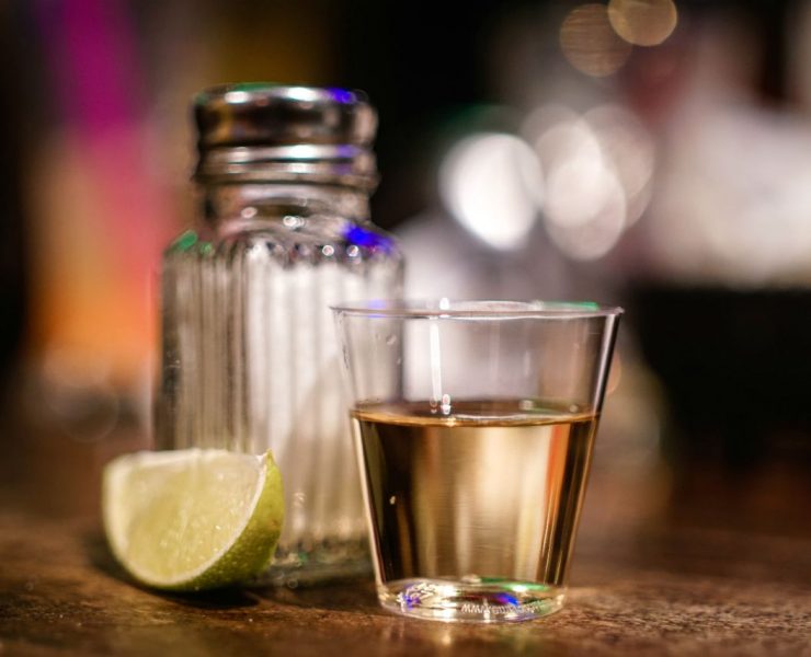A shot glass of tequila is on a table next to a lime wedge and a salt shaker.