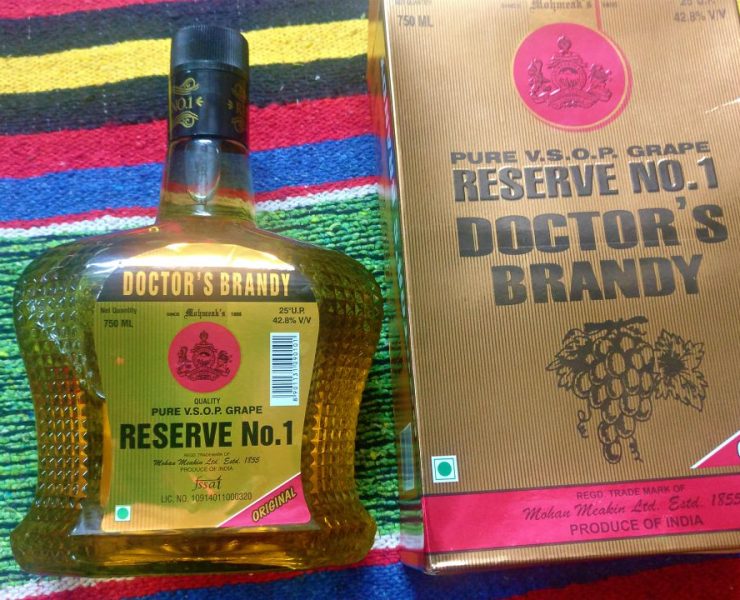 A bottle and box of Doctor's Brandy, labeled "Pure V.S.O.P. Grape Reserve No.1." The bottle is on a colorful striped background.