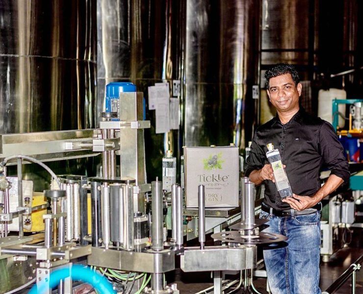 A person stands in a factory near machinery, holding a product.