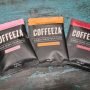 Three Coffeeza single-serve pour-over coffee packets displayed on a textured blue surface. Flavors: Light Roast, Medium-Dark Roast, Dark Roast.
