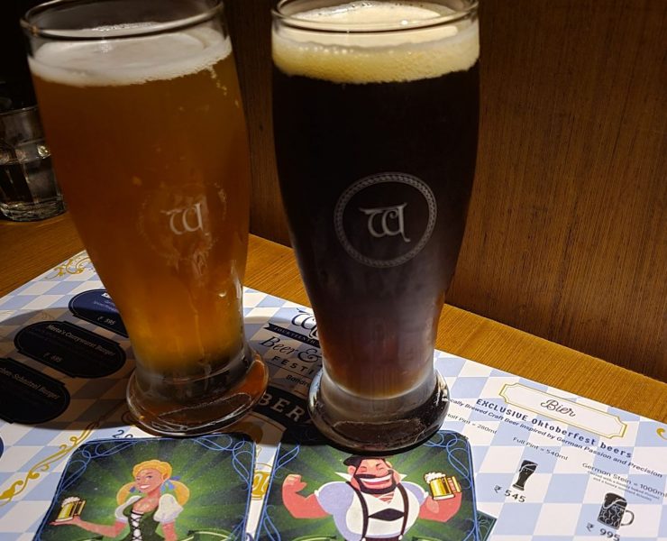 Two glasses of beer, one light and one dark, on a table with illustrated coasters and a menu beneath them.