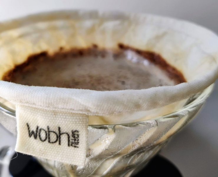 Close-up of a coffee dripper with a cloth filter labeled "wobt filter," containing ground coffee and water.