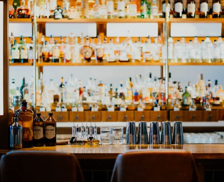 Bar counter with various bottles on shelves in the background, cocktail shakers, and glasses neatly arranged on the surface.