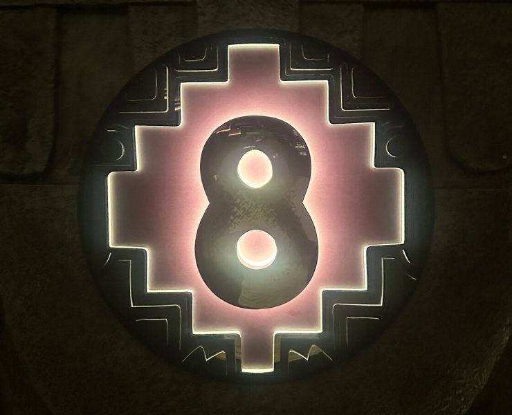 Illuminated number 8 on a circular sign with a geometric design and a pink glow, set against a dark background.